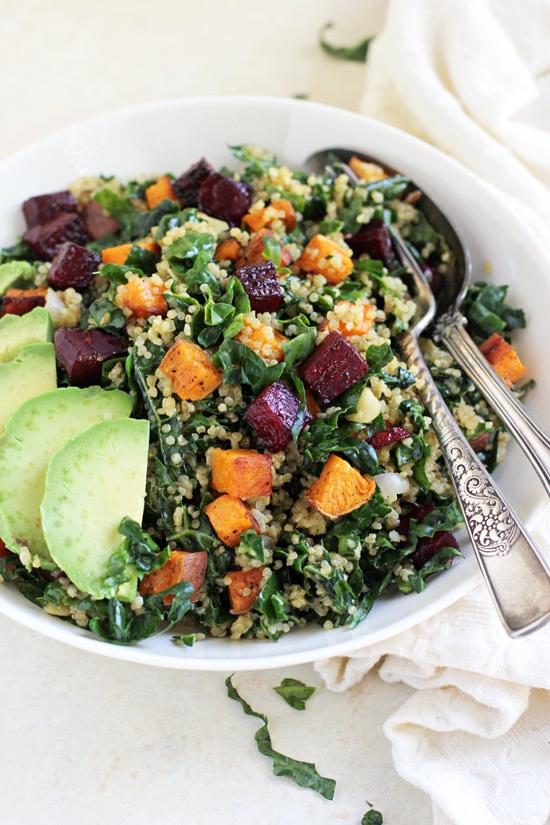 Side angle view of Kale and Quinoa Rainbow Salad in a bowl with a fork and spoon.