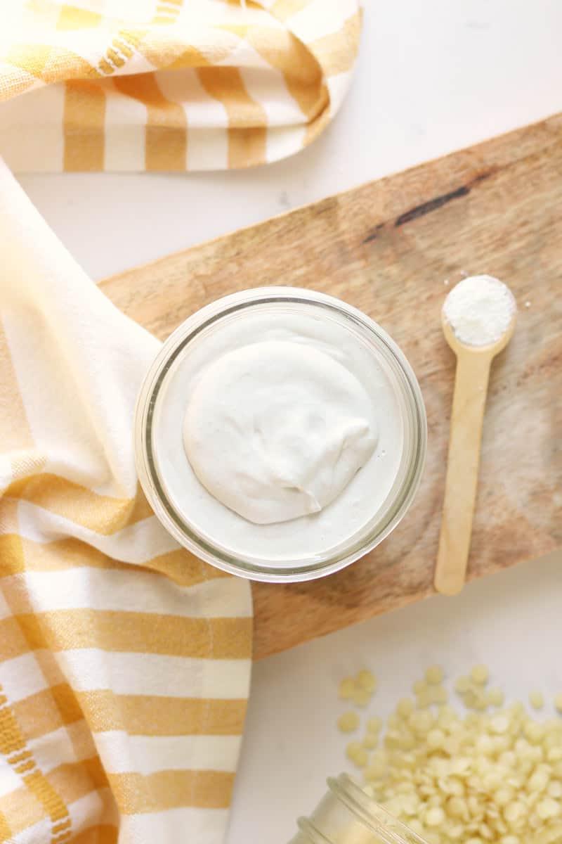 a jar of homemade diaper rash cream with dried lavender flowers and a spoonful of zinc oxide next to it on a wooden cutting board
