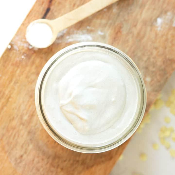 a jar of homemade diaper rash cream with dried lavender flowers and a spoonful of zinc oxide next to it on a wooden cutting board