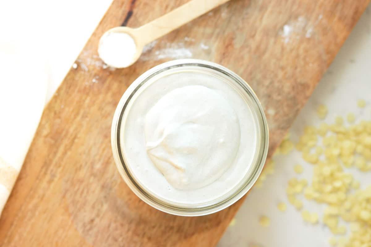 a jar of homemade diaper rash cream with dried lavender flowers and a spoonful of zinc oxide next to it on a wooden cutting board