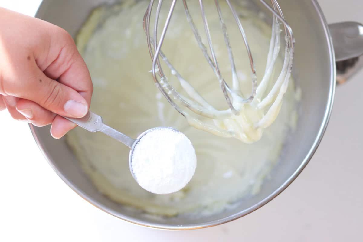 a tablespoon of zinc oxide powder being added to a kitchenaid mixer of homemade diaper rash cream