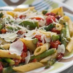 Cooked penne pasta, 1-inch pieces of asparagus, grape tomatoes, topped with a garnish of parmesan cheese on a white plate with blue and brown stripes